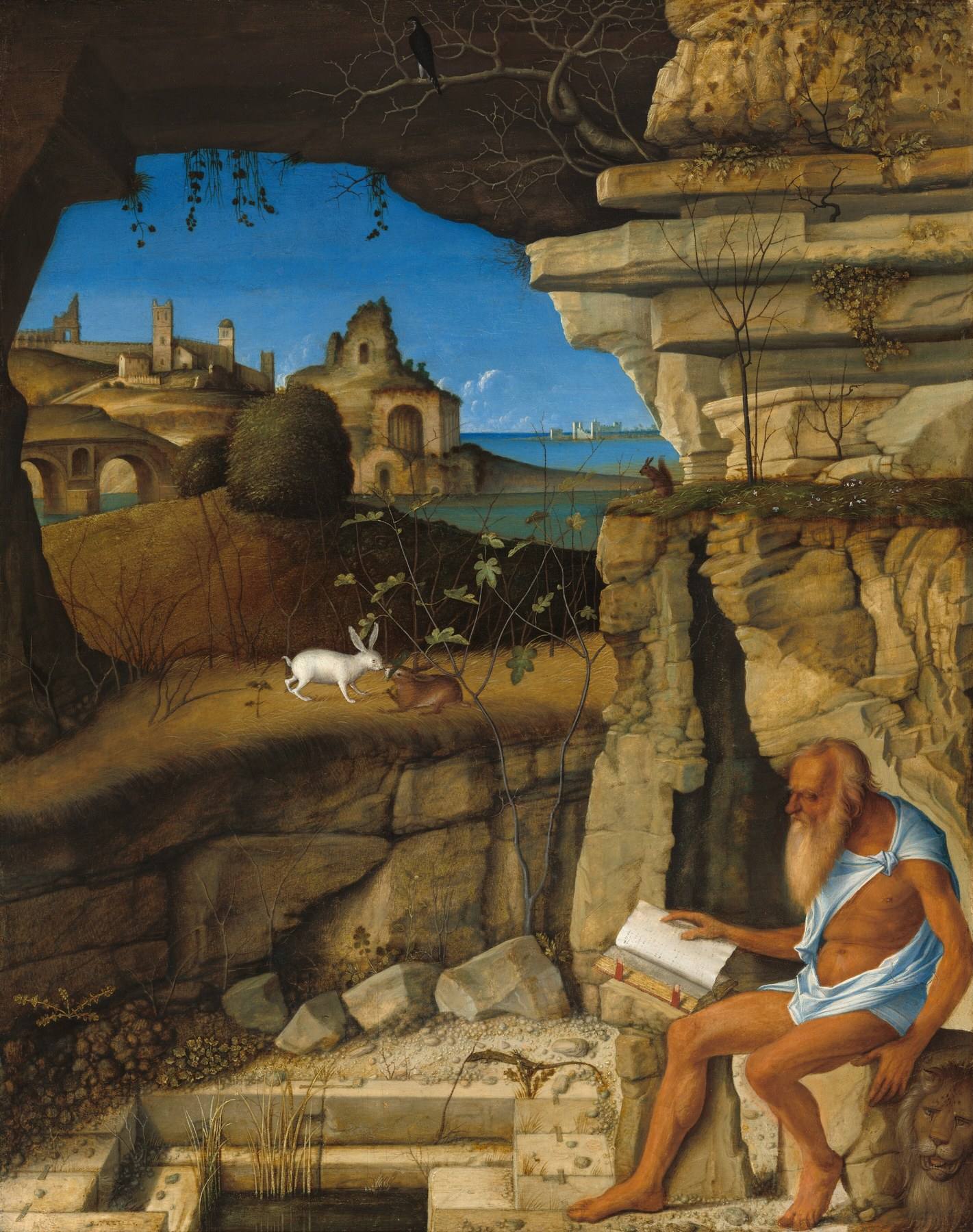 Giovanni Bellini’s painting of a white-bearded old man in a pale blue cloth, seated barefoot on a rock at the mouth of a cave and reading a large book propped open on a ledge, a lion lying beside him and two rabbits, stone buildings and blue water in the sunlit landscape beyond.